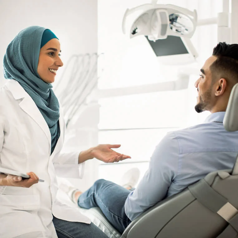 Muslimische Zahnärztin mit Charly-Apps Tablet redet mit einem Patient in der Zahnarztpraxis